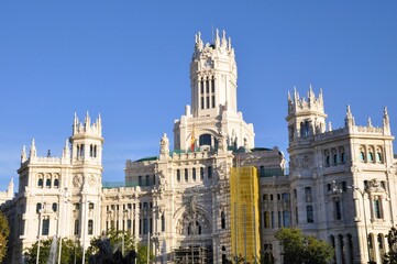 Fototapeta premium The impressive Palacio de Cibeles in Madrid, bathed in golden sunlight, showcasing its elaborate Neo-Gothic architecture under a clear blue sky.