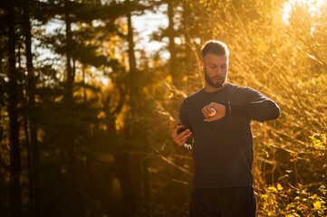 Male athlete checking smartwatch during training in autumn forest