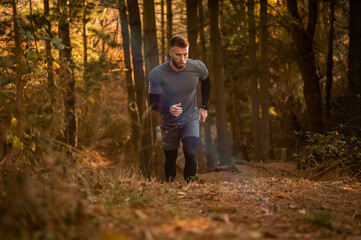 Determined male athlete running uphill in autumn forest