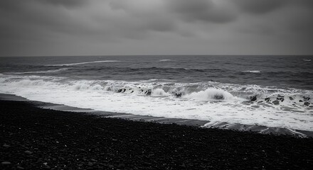 Dramatic black and white image of ocean waves crashing on the shore under a stormy sky