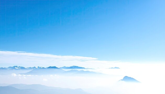 A panoramic view of a mountain range partially obscured by a layer of mist or clouds under a clear blue sky.  The mountains appear hazy in the distance, creating a serene and tranquil atmosphere
