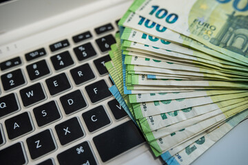 Euro banknotes lying on a laptop keyboard, representing digital finance and modern economy
