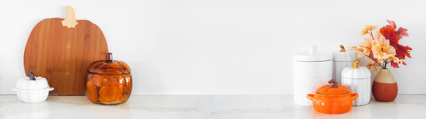 Fall pumpkin theme kitchenware on a white stone countertop. Banner against a white wall background...