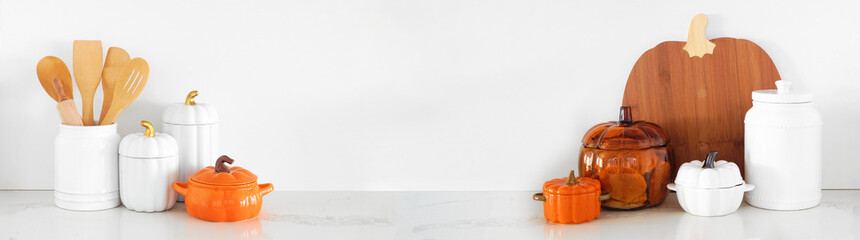 Autumn pumpkin theme kitchenware and utensils on a white stone countertop. Banner against a white...