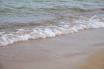 Wave splashing on sandy beach, clear Baltic sea water, foam, natural coastline. Bright outdoor scene, travel, summer, relaxation, peaceful nature
