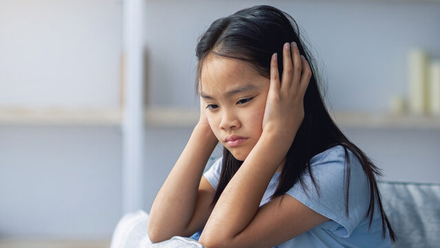 Mother daughter conflict. Young korean mother trying to speak to her upset daugter, sitting on sofa at home. Offended asian girl covering her ears, not wishing to listen to parent - Powered by Adobe