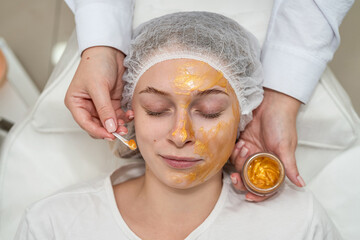Woman enjoying soothing pampering golden facial mask by beautician at spa salon