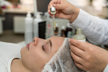 cosmetologist holds a pipette with essential oil on face of patient girl.