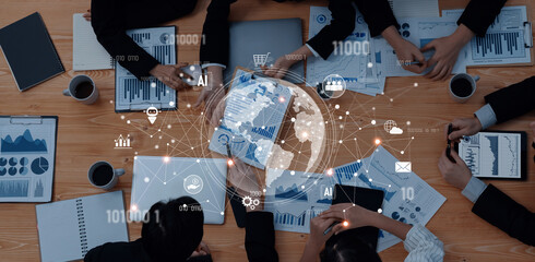 A team of professionals engages in a collaborative business meeting, analyzing data on charts and documents while surrounded by technology and global connectivity visuals. Trope