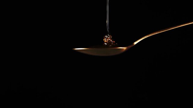 Spoon Full of Honey Against a Black Background Being Filled From Above