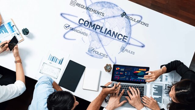 A diverse team collaborates on a compliance strategy, utilizing data visualizations and technology in a modern office environment, focusing on global regulations and policies. Raster
