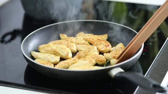 Woman frying chicken fillet in a pan at home kitchen, preparing a simple homemade meal.