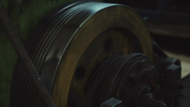 Close up view of a metal pulley with a v belt spinning on an old industrial machine, showcasing the mechanical rotation and movement of heavy equipment inside a vintage workshop or factory