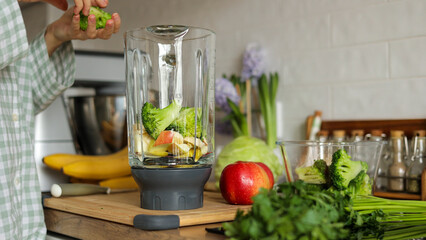 Unknown woman makes healthy detox breakfast smoothie at home. Female hands throws parsley in blender bowl, prepares fresh green vegetarian fruit-greens-vegetables drink to cleanse, provide energy body
