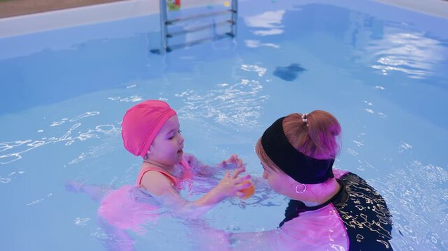 caregiver and toddler enjoy pool fun, gentle splashes, laughter, guidance, safe learning, playful bonding, toys floating nearby, relaxed movement, smiles, early swim lesson in warm light