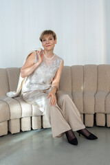 Smiling woman sitting on sofa in bright sunny room. Looking at camera. Vertical photo. High quality photo