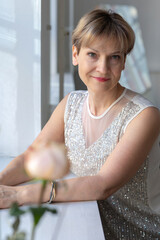 Portrait of smiling woman in festive clothes against a gray wall in a bright sunny room. Vertical photo. High quality photo