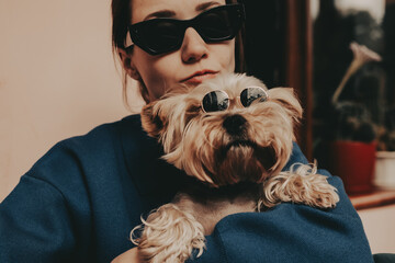 Trendy woman wearing black sunglasses holding a stylish Yorkshire Terrier dog in mini round...