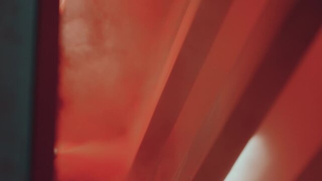 Close up of a spray gun applying red powder coating to a complex metal part in a factory setting, with the electrostatic process creating a uniform and durable finish on the steel surface