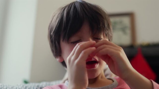 Young boy rubbing eyes with both hands, showing signs of tiredness and sleepiness in everyday family home environment indoors