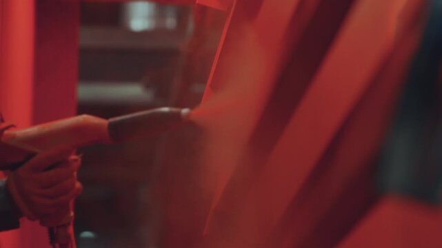 Professional painter in a workshop applying red powder coat paint to a metal structure with a spray gun, an industrial electrostatic process for finishing and surface protection