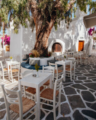 Greece white architecture cobblestone street flowers cafe with colorful chairs, Naoussa, Paros island