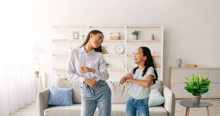 Obraz premium Full length of asian mother dancing to music with her cute daughter at home, having fun together. Mom and her kid enjoying favorite song together, fooling around in living room
