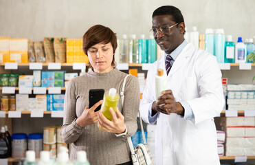 Woman in pharmacy scans QR code on antidandruff shampoo, studies item in detail, collects information online, uses quick link to access drugs instructions. African man pharmacist offer available