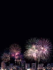 Colorful fireworks illuminate the night sky over a city skyline. Bright bursts of light in various colors create a festive atmosphere.