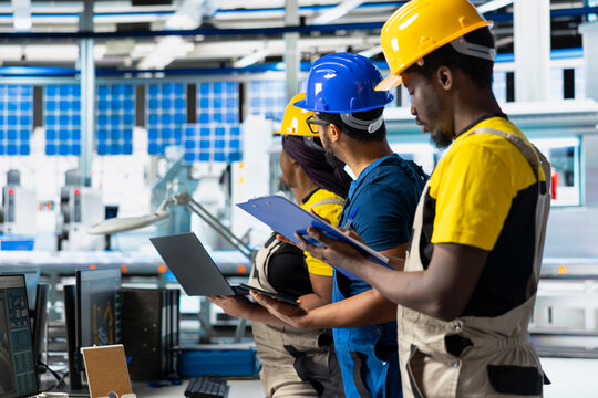 African american workers checking up on manufacturing equipment in solar panel factory, reading documentation files. Team of engineers in industrial facility inspecting production process.