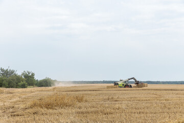 Harvesting Process in a Wide Open Field with Heavy Machinery Collecting Bales of Straw Under a Slightly Overcast Sky in a Rural Agricultural Landscape
