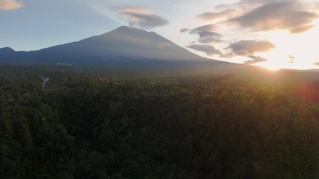 Aerial view drone real time Beautiful shot of Mount Agung in Bali during a golden sunset, overlooking a lush tropical forest.
