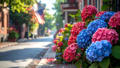 A picturesque street scene lined with vibrant red, pink, and blue hydrangeas, with a blurred flag waving. The focus is on the flowers