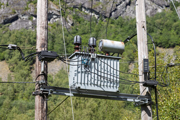 Utility pole with power transformer and intricate electrical wiring against a rugged mountain and...