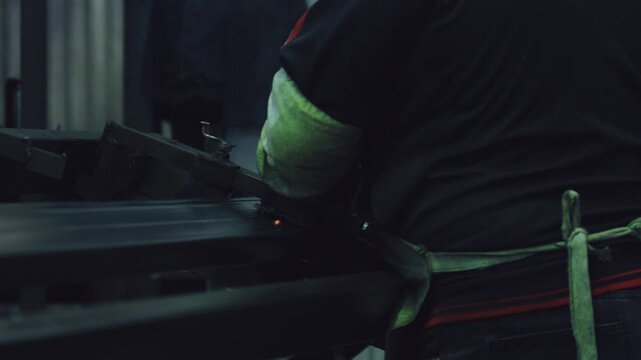 Industrial worker in protective gloves welding steel components in a workshop. Bright sparks and smoke flying from the hot metal during the fabrication process in the manufacturing plant