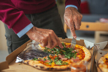 Senior man hands cutting pizza in delivery box