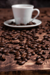 Roasted coffee beans on a wooden surface close to a coffee cup.