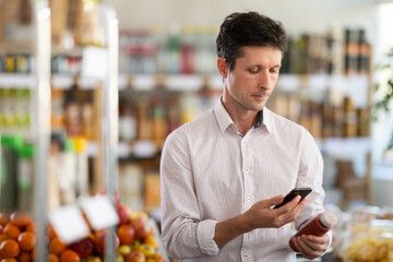 Adult man buyer scanning qr code for red smoothie in bottle in grocery store