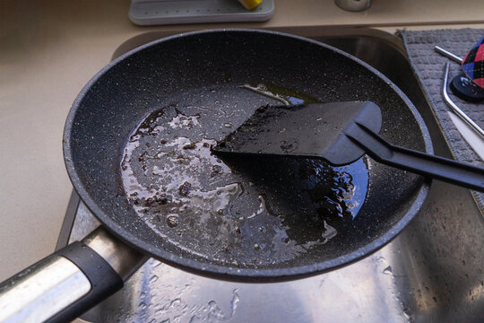 Nonstick pan with hot oily and greasy residue in sink, black spatula nearby, start of cleaning process, cleaning kitchen concept