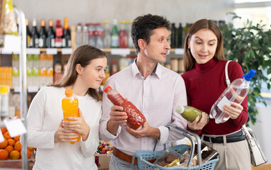Couple adult man and young woman with teenage daughter choosing drinks in grocery store