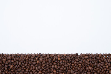A close up of coffee beans on a white background. The beans are scattered in a way that creates a sense of depth and texture. Concept of warmth and comfort