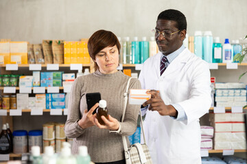 Obraz premium Adult woman buyer scanning qr code for medicinal syrup with adult man pharmacist in pharmacy