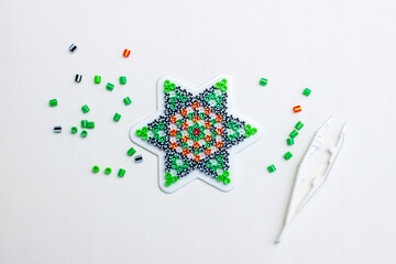 Colorful thermo mosaic beads arranged on star template with tweezers, kids DIY craft game, creative toy for children on white background