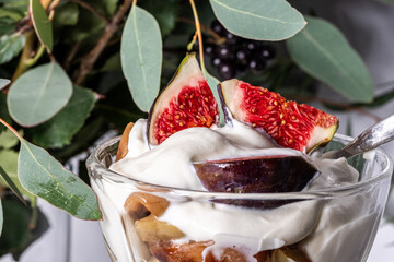 Fresh dessert featuring creamy yogurt topped with ripe figs and plums, garnished with green leaves,...