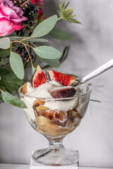 Delicious dessert featuring creamy yogurt topped with fresh figs and caramelized fruits in a glass bowl, surrounded by vibrant flowers and greenery, showcasing a delightful culinary experience