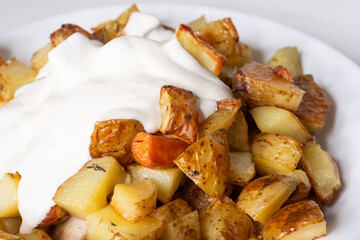 Golden roasted potatoes topped with creamy sauce, served on a white plate, showcasing a delicious and hearty dish perfect for any meal or culinary presentation