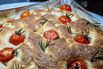 Freshly baked focaccia topped with cherry tomatoes and rosemary, showcasing a golden crust and fluffy dough, perfect for traditional culinary experiences and delicious meals