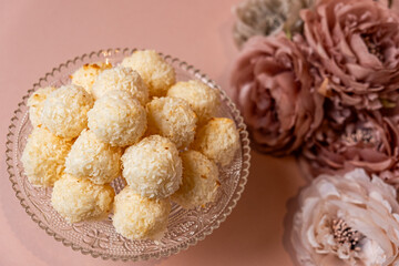 Delicious coconut balls arranged in a decorative glass bowl, surrounded by soft pink flowers, creating an inviting and elegant dessert presentation for special occasions