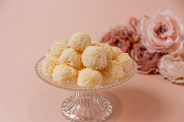 Delicious coconut balls arranged on a crystal plate, surrounded by soft pink flowers, creating an inviting and elegant dessert display for special occasions