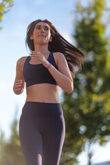 Young woman jogging on a sunny day along a tree-lined pedestrian path in a vibrant urban setting